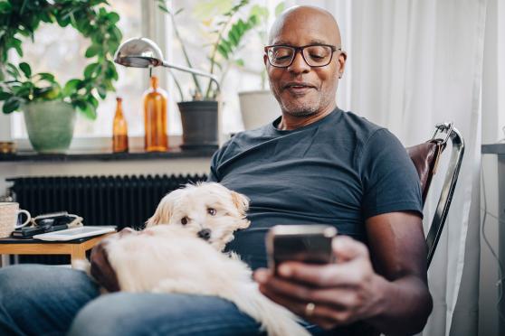 Man looking at his phone with a small dog on his lap